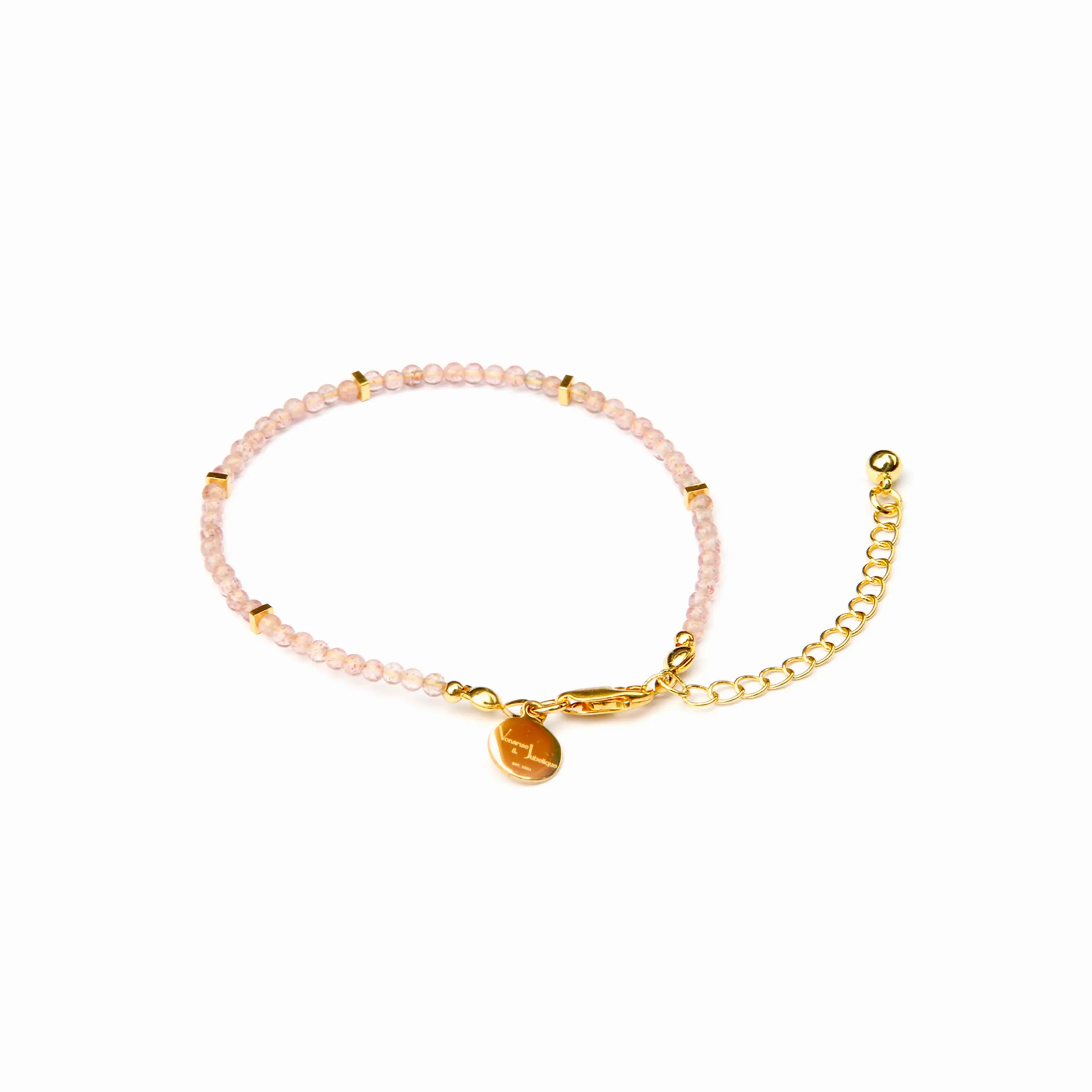 A delicate beaded bracelet with light pink faceted beads, gold spacer accents, a gold lobster clasp, an adjustable gold chain extender, and a small round gold charm, shown on a plain white background.