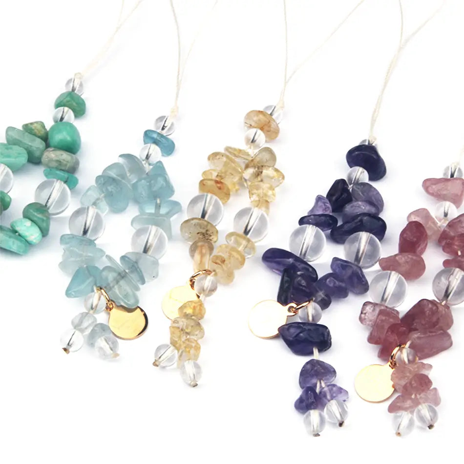 Four beaded gemstone necklaces with clear faceted beads and small gold disc charms, shown in green, aqua, yellow, and purple on a white background.
