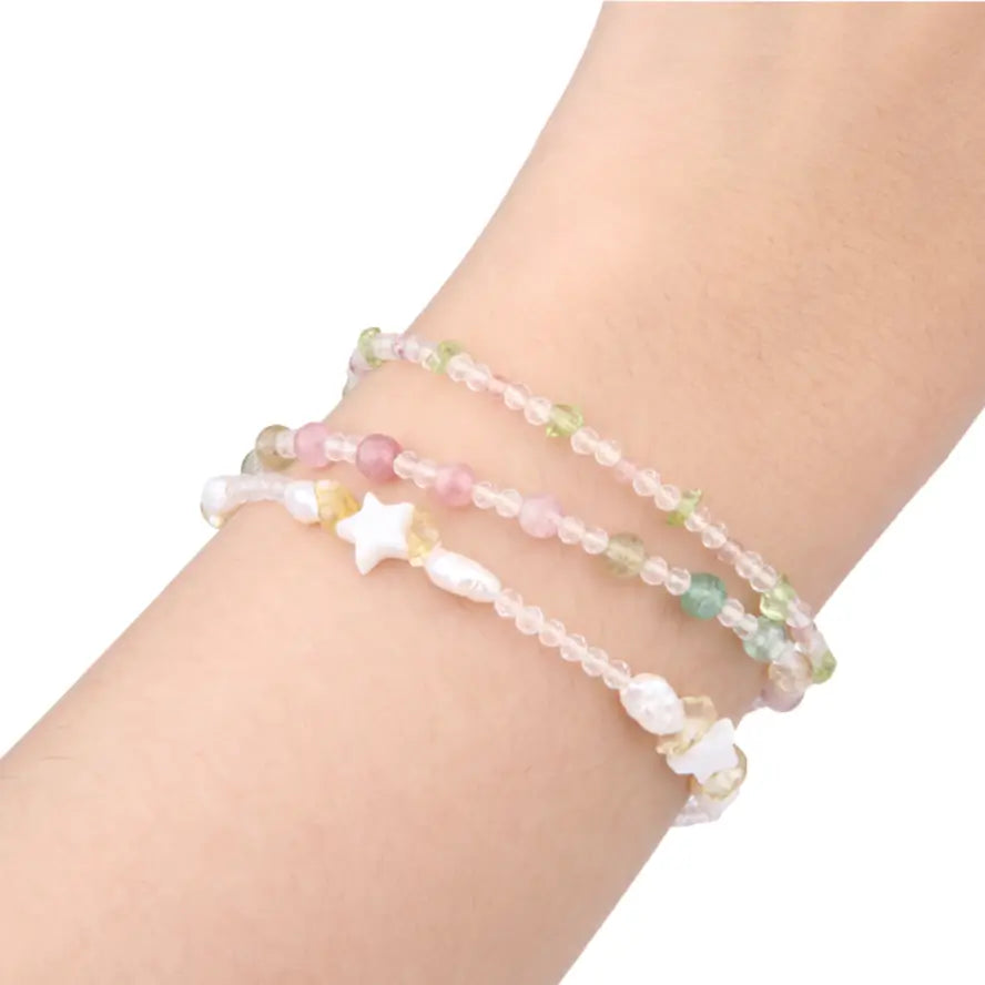 Three delicate beaded bracelets with pastel pink, green, and white beads, including a white star charm and pearl accents, shown worn on a person's wrist against a white background.