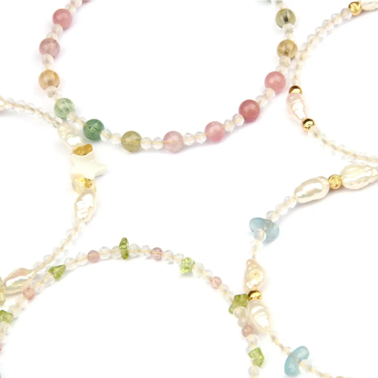 A close-up of delicate beaded jewelry strands on a white background, featuring translucent white beads, pastel pink, green, and blue stones, and small gold spacer beads.