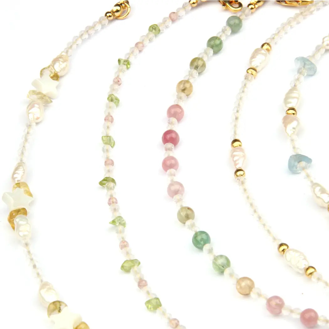 Four beaded strands of jewelry laid out on a white background, featuring small translucent beads in pink, green, blue, and gold-tone accents.