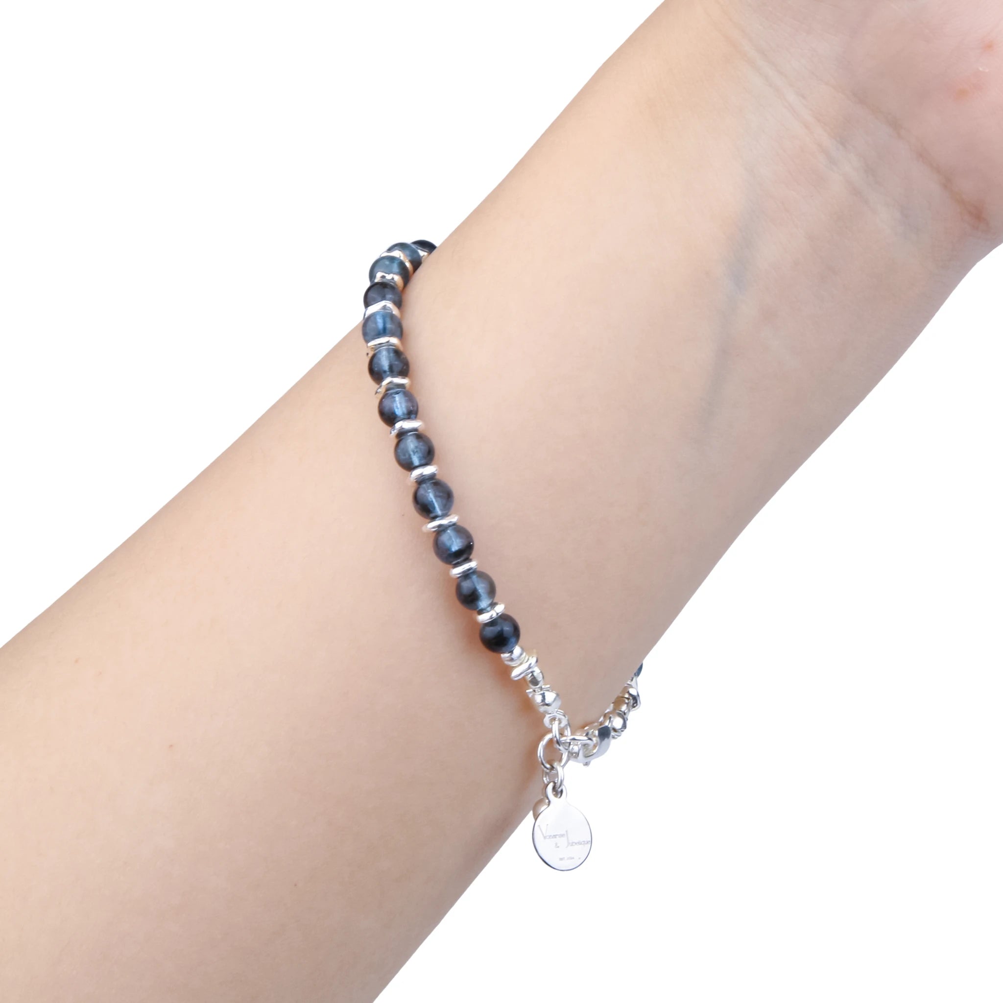 A beaded stretch bracelet with dark blue-gray beads and silver spacer rings, worn on a person's wrist with a dangling silver charm, shown against a plain white background.